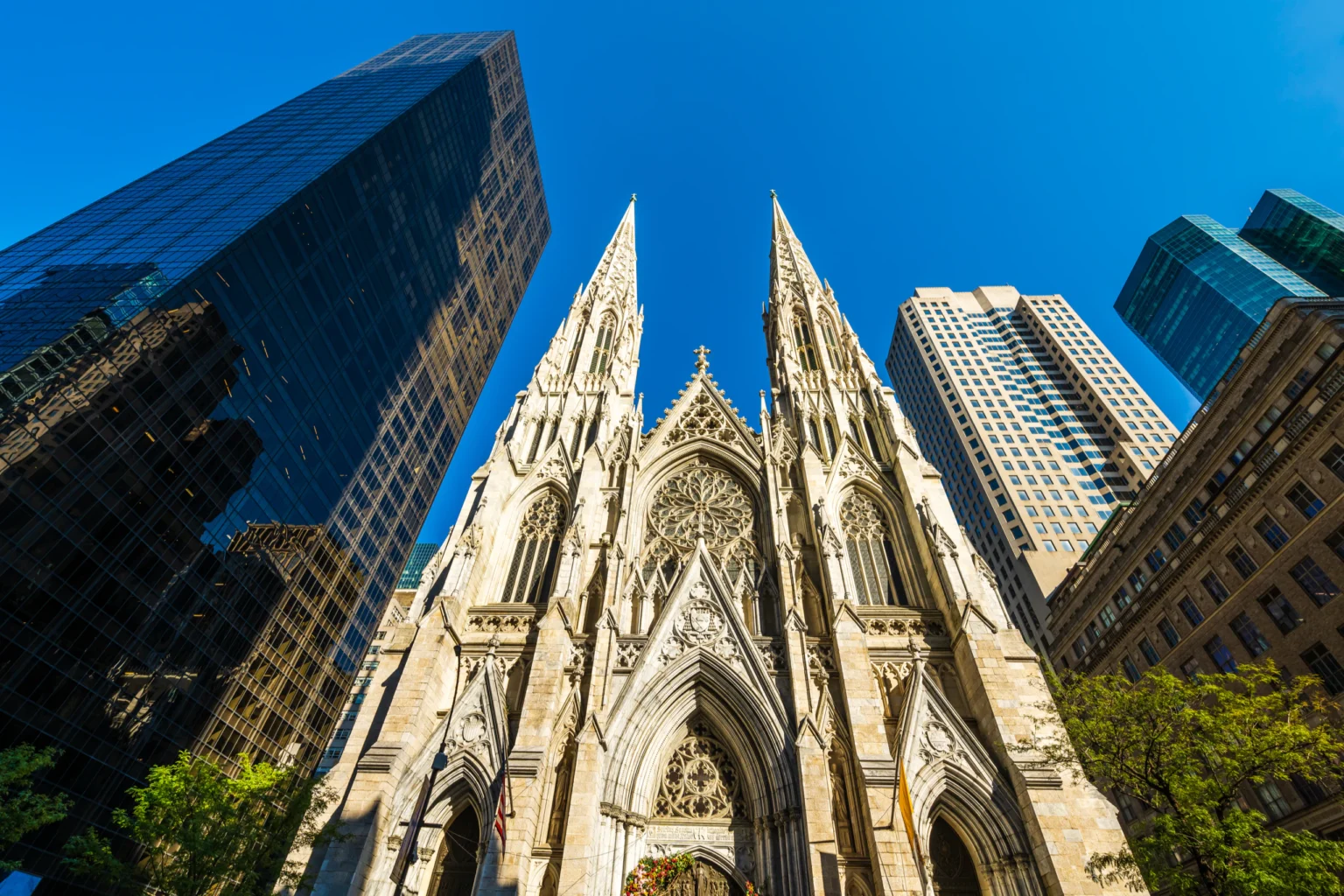 Twin Gothic cathedral spires rising between glass skyscrapers against a blue sky