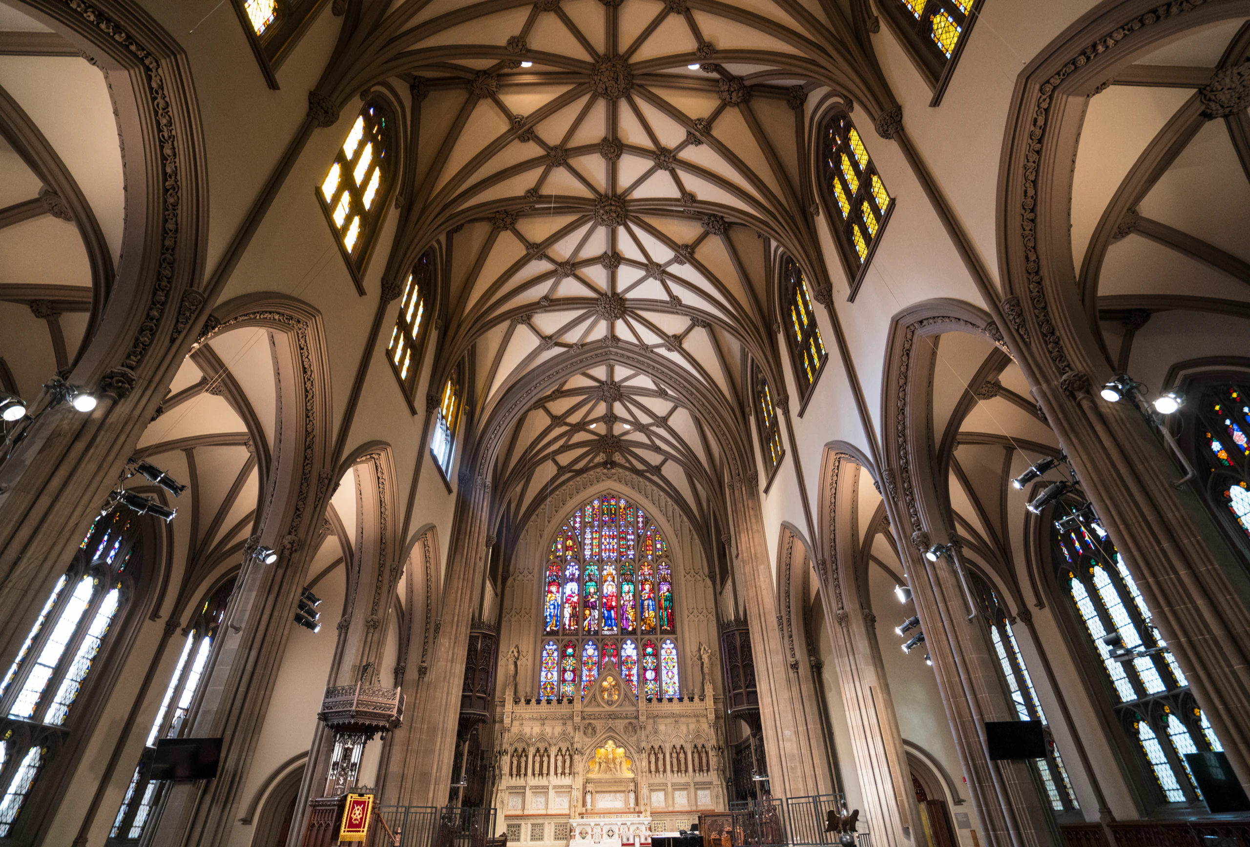 Looking up at the ribbed vaulted ceiling of a Gothic church, with a stained glass window above the altar